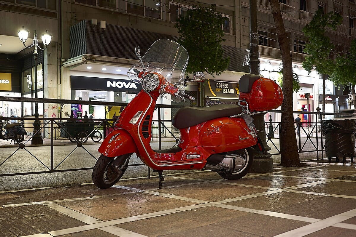 Vespa GTS 300 rouge garée dans une rue commerçante éclairée de nuit