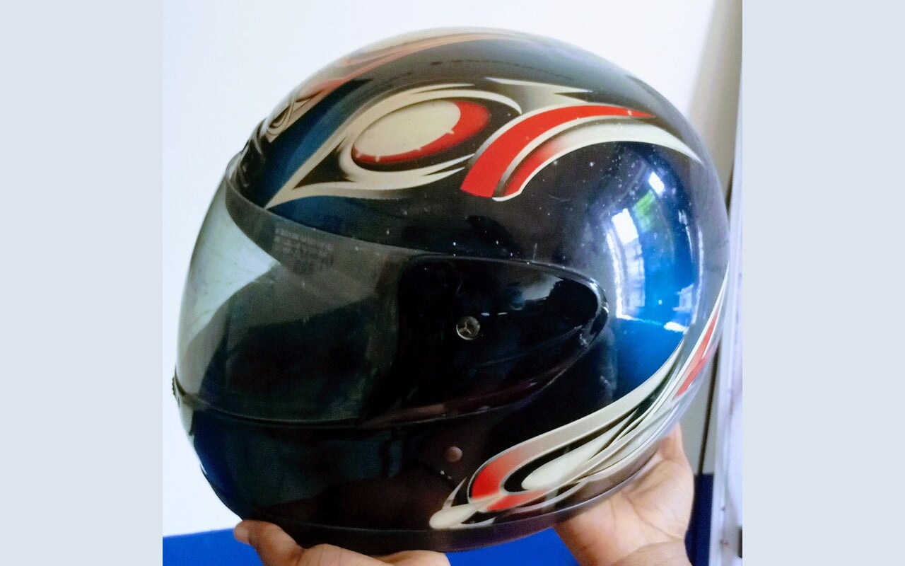 Casque moto intégral tenu à la main, visière teintée fermée, décoration noire rouge et blanche
