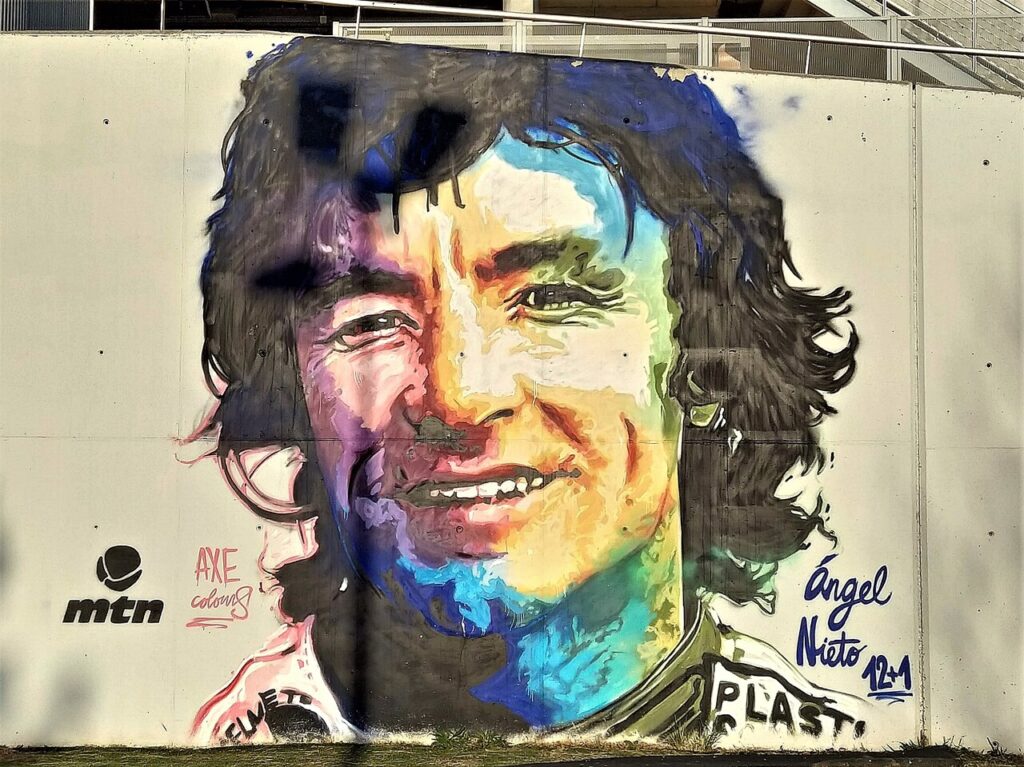 Une fresque murale rend hommage à Ángel Nieto avec la mention « 12+1 », clin d'oeil au chiffre 13 qu'il refusait de prononcer pour ses treize titres mondiaux. (Photo : Alberto-g-rovi, CC BY 3.0, via Wikimedia Commons.)