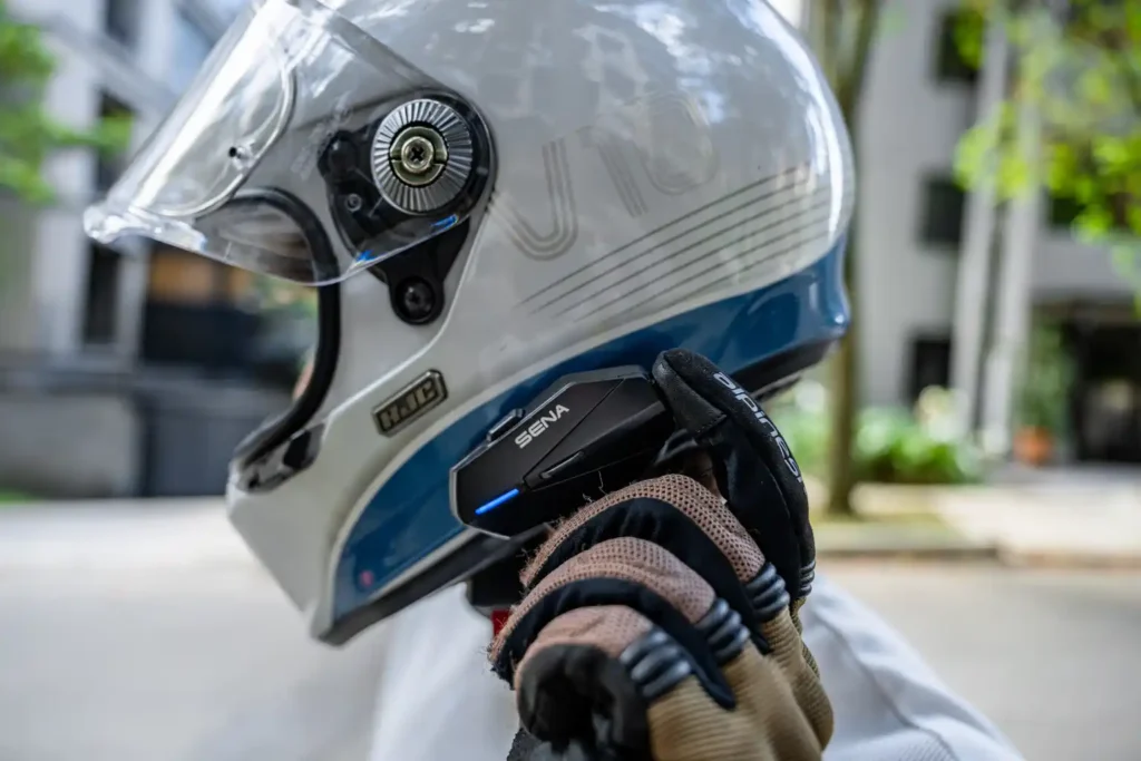 Motard portant un casque intégral carbone équipé d'un intercom Sena Apex, main gantée sur la molette de commande (Source : Sena)