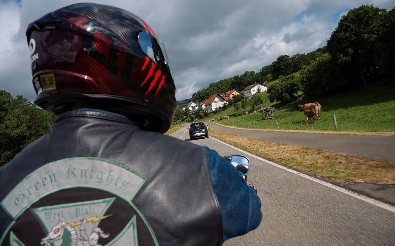 Motard roulant sur une route de campagne, vu par-dessus son epaule