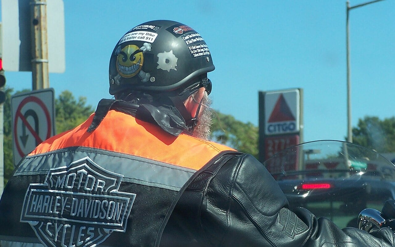Motard portant un casque bol couvert d'autocollants au guidon d'une Harley-Davidson