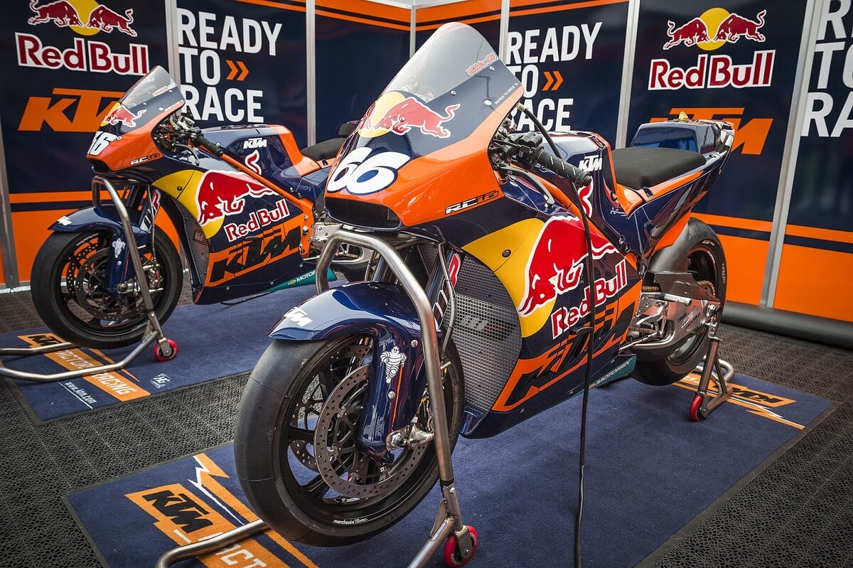 Deux motos de MotoGP KTM RC16 sur béquilles dans le box de l'équipe, devant des panneaux Red Bull